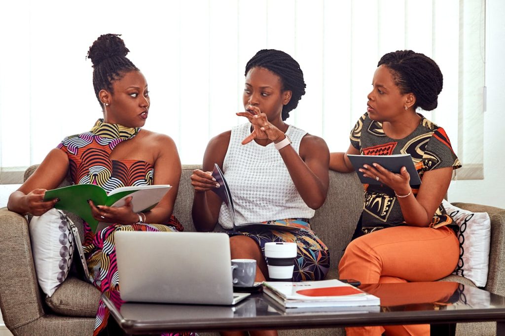 women-talking-to-each-other-3894383 Three African American women engaged in a collaborative business meeting indoors.